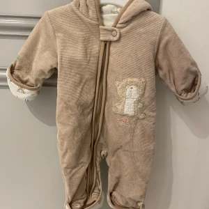 Beige overall i storlek 62 - Beige overall i storlek 62. Overallen har vantar och skydd för fötterna att ta fram vid behov.