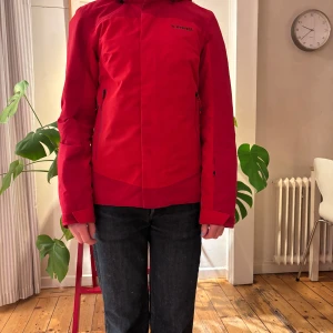 Röd skidjacka från Everest storlek 34 i nyskick - Denna skidjacka är en stilsäker och varm skid- och snowboardjacka, designad för att hålla dig bekväm och skyddad i backen. Jackan är vadderad med återvunnen polyester som effektivt håller dig varm, medan det mjuka 20D nylonfodret mot huden ger en lätt och behaglig känsla, perfekt för långa dagar i kallt väder. Det följsamma yttermaterialet i twillväv gör jackan smidig att röra sig i, samtidigt som den erbjuder ett vind- och vattentätt skydd på upp till 5 000 mm vattenpelare. 