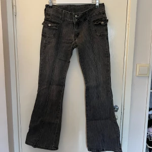 Svarta bootcut jeans från brandy melville med fickdetaljer - Snygga svarta bootcut jeans ”agatha jeans” med framträdande fickdetaljer och knappar. De har en lågmidjad passform och är perfekta för en avslappnad stil. Jeansen har en klassisk look med en modern twist. 