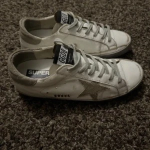 Vita sneakers med stjärndetalj - Snygga vita sneakers med en grå stjärndetalj på sidan och matchande grå snörning. Skorna har en klassisk design med låg profil och är perfekta för en avslappnad stil.