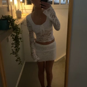 Vitt spets set - Säljer ett elegant vitt set med långa ärmar och en fin knytning framtill. Kjolen har en kort längd och är perfekt för speciella tillfällen. Den har en vacker spetsdesign. (Det är ett set så tröja och kjol ingår) säljer pga beställde för liten storlek och gått för många dagar för att returnera!