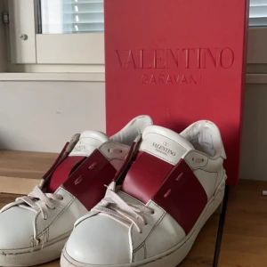 Valentino Garavani sneakers - Snygga Valentino Garavani sneakers i vitt med röda detaljer. Skorna har en klassisk design med snörning och en stilren look. Perfekta för att ge din outfit en lyxig touch.
