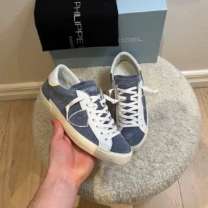 Blå och vita sneakers från Philippe Model - Snygga sneakers i blått och vitt från Philippe Model. Skorna har en klassisk design med snörning och en bekväm sula. Perfekta för en stilren look.