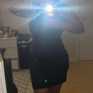 Svart glittrig klänning - Snygg svart klänning med glittriga detaljer. Den har en oneshoulder-design som ger en elegant look. Perfekt för en kväll ute eller en speciell tillställning.