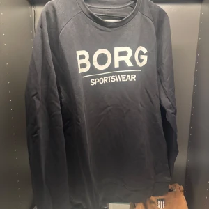 Svart tröja från Björn Borg - Säljer en svart tröja från Björn Borg med texten 'BORG SPORTSWEAR' på framsidan. Tröjan har långa ärmar och en rund halsringning. Perfekt för en sportig look eller avslappnad stil.