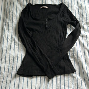 Svart ribbad topp från Anna Field - Snygg svart ribbad topp från Anna Field med långa ärmar och knappar framtill. Perfekt för en stilren look 💕