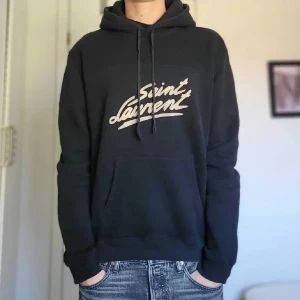 Saint laurent hoodie  - Säljer nu denna riktigt snygga och eftertraktade saint laurent hoodie i storlek S. Den är i grymt skick förutom två små hål/lagningar som inte märks vid användning. Skriv vid fler frågor eller bilder!