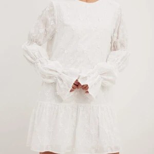 Studentklänning / vit kort klänning från NAKD - Säljer en av mina studentklänningar. Jag bara använt den en gång, och den har inga täcken på användning. Den har blomsterdetaljer, puffärmar och är djup i ryggen😊