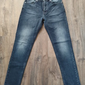 Mörkgrå jeans Steady Eddie II - nya!  - Snygga mörkgrå jeans från Nudie Jeans, modell Steady Eddie II. De har en klassisk femficksdesign och knappar i gylfen. Perfekta för en avslappnad stil med en modern Touch. Helt nya, inköpt för 2499kr.