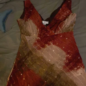 Färgglad topp från Next - Säljer en färgglad topp från Next i en mix av röd och beige. Klänningen har en v-ringad design och är dekorerad med små paljetter som ger en glittrig effekt. Perfekt för att sticka ut med stil!