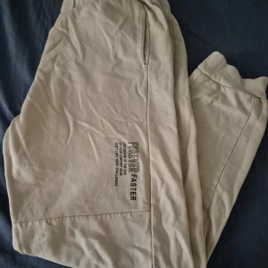 Beige mjukisbyxor med tryck - Säljer ett par bekväma beige mjukisbyxor med tryck på sidan. Perfekta för en avslappnad stil. Byxorna har en elastisk midja och är gjorda i ett mjukt material.