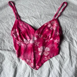 Rosa blommig sommartopp  - Rosa topp från bershka med blommiga detaljer och smala axelband. Perfekt till sommaren! Toppen är väldigt kort och är ”triangelformad” framtill! Använd ett fåtal gånger🫶