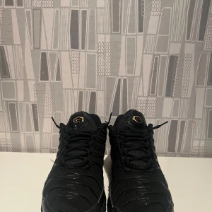 Svarta sneakers med gulddetaljer - Snygga svarta sneakers med gulddetaljer och snörning. Skorna har en sportig design med en synlig luftdämpning i sulan för extra komfort. Perfekta för en stilren look.