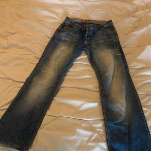 Blå jeans från D&G - Snygga blå jeans från D&G med slitna detaljer och en klassisk femficksdesign. De har en knappgylf och bälteshällor, perfekt för en avslappnad stil.