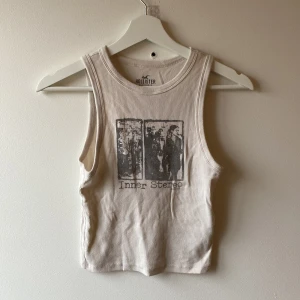   linnetopp från Hollister - Säljer en beigevit ribbad linnetopp från Hollister med tryck av texten 'Inner Stereo' och ett grafiskt motiv på framsidan. 
