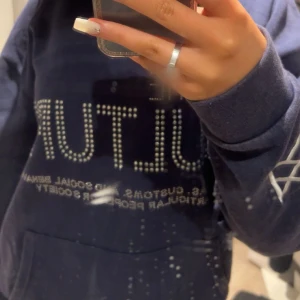 Mörkblå hoodie med textdetaljer - Säljer en mörkblå hoodie med textdetaljer i vitt och en stor ficka framtill. Perfekt för en avslappnad stil. Hoodien har långa ärmar och en bekväm passform💕