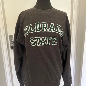 Mörkgrå sweatshirt med Colorado State-tryck - Säljer en mörkgrå sweatshirt från Champion med tryck i vitt och grönt på framsidan. Tröjan är perfekt för skolan eller bara en chill  outfit