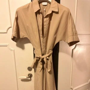 Skjortklänning, Vila - Säljer denna fina beige klänningen som aldrig är använd och bara står i min garderob. Jag är 162 cm och på mig går den ner till knäna så perfekt längd för den som inte vill ha för lång eller kort klänning. Köpt från Vila i butik och är i nyskick🤎