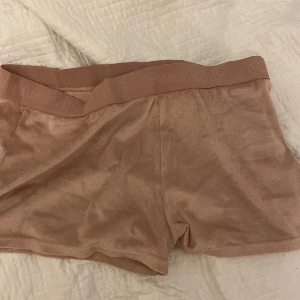 Säljer ett par snygga beige shorts från Juicy Couture i storlek XL. De är gjorda i ett mjukt material och har en elastisk midja med Juicy Couture-loggan. På baksidan finns texten 'Juicy' i glittriga stenar. Perfekta för en avslappnad dag eller en mysig hemmakväll!. Shorts.