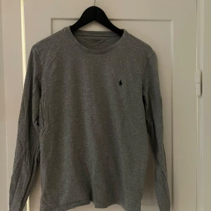 Grå långärmad tröja från Polo Ralph Lauren - Säljer en stilren grå långärmad T-shirt från Ralph Lauren. Den har en klassisk passform och är perfekt för både vardag och lite mer avslappnade tillfällen. Tröjan är i bomull och har en liten broderad logga på bröstet. Superbekväm och lätt att matc
