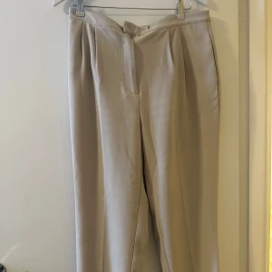 Beige byxor från NA-KD - Säljer ett par stilrena beige byxor från NA-KD. De är högmidjade med en rak passform och har en diskret dragkedja framtill. Perfekta för både vardag och fest! 