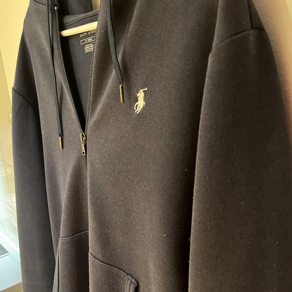 Säljer en snygg och bekväm mörkblå hoodie från Ralph Lauren. Den har en dragkedja framtill och en klassisk logga på bröstet. Perfekt för kyliga dagar eller som ett stilrent lager under jackan. Den har långa ärmar och en praktisk huva. Öppen för byten. Tröjor & Koftor.