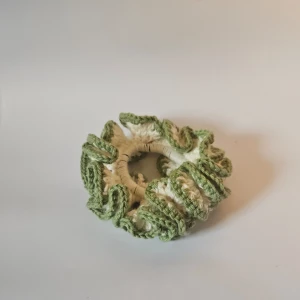 Grön stickad scrunchie - Säljer en superfin grön virkad scrunchie som är perfekt för att piffa upp vilken frisyr som helst. Den har en mysig och unik design med volanger som ger en extra touch. Perfekt accessoar för både vardag och fest!