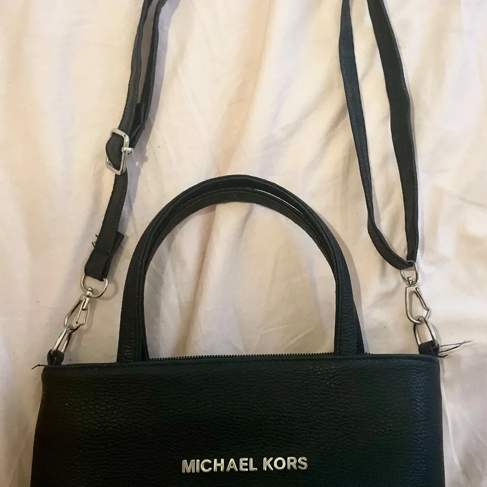 Säljer en snygg svart handväska från Michael Kors. Väskan är i läder och har en stilren design med silverfärgad logga på framsidan. Den har både handtag och en justerbar axelrem, vilket gör den superpraktisk. Insidan är fodrad med ett mönstrat tyg! . Väskor.