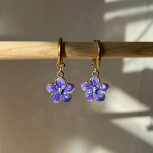 Lila blommiga örhängen - Superfina örhängen med lila blommor som hänger från en guldfärgad ring. Perfekta för att ge en färgklick till vilken outfit som helst. Blommorna har en söt och detaljrik design som verkligen fångar ögat. Passar både till vardags och fest! Handgjorda.