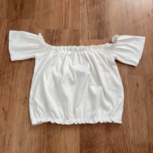 Vit offshoulder topp från Bik Bok - Säljer en söt vit offshoulder topp från Bik Bok i ribbat material. Toppen har korta ärmar och en elastisk kant upptill och nedtill för en bekväm passform. Perfekt för varma sommardagar!