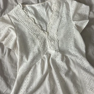 Vit blus med spetsdetaljer - Säljer en söt vit blus med v-ringad spetsdetalj och korta ärmar. 