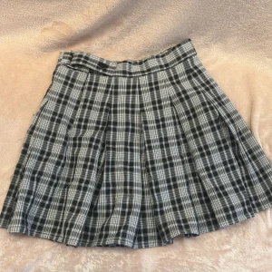 Rutig kortkjol med knappar - Snygg rutig kortkjol i svart och vit med knappar i midjan. Perfekt för en stilren look med en twist. Kjolen har ett klassiskt rutmönster och är lätt att matcha med olika toppar.