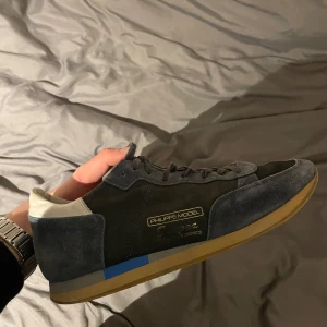 Grå blåa sneakers från Philippe Model - Tjena! säljer mina snygga grå/blå sneakers från Philippe Model med en stilren design. Skorna har en ovandel i mocka och skinn, med vita detaljer på hälen och en gummisula i beige. Perfekta för en avslappnad stil.