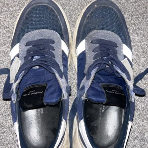 Blå sneakers från Philippe Model Junior - Snygga blå sneakers från Philippe Model Junior med vita detaljer. Skorna har en klassisk snörning och en stilren design som passar perfekt för en avslappnad look. De är tillverkade i en kombination av material som ger både komfort och stil. Skorna kommer tvättas av noga och rätt innan leverans.