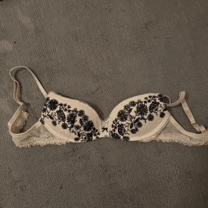Intimissimi  bh beige med svart broderi - Intimissimi bh endast använd 1 gång säljes då den är för liten. Storlek 75b. Nypris 499 lag mitt pris 270 kr. Elegant beige bh med vackert svart blommigt broderi. Den har justerbara axelband och spetsdetaljer längs kanterna för en feminin touch.
