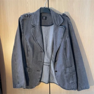 Grå jeansjacka från GR Design - Snygg grå jeansjacka från GR Design med klassisk krage och knappar framtill. Jackan har långa ärmar och praktiska fickor. Perfekt för en avslappnad stil. Storlek M