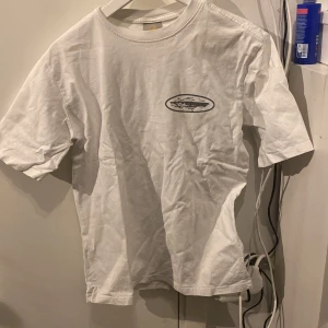 Vit t-shirt med tryck från cortiez  - Säljer en vit t-shirt med ett tryck av en krokodil och texten 'DOWN UNDA' på baksidan. T-shirten har korta ärmar och en rund halsringning. Perfekt för en avslappnad stil.