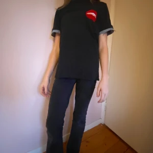 Svart t-shirt med röd detalj - Snygg svart t-shirt med en röd detalj på bröstet, och denim design på ärmarna. T-shirten har korta ärmar och en normal passform. Perfekt för en avslappnad stil.