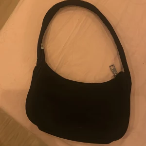 Svart axelväska med dragkedja - Snygg svart axelväska med en enkel design och praktisk dragkedja. Perfekt för att bära dina dagliga nödvändigheter med stil. Väskan har en bekväm axelrem och en minimalistisk look.