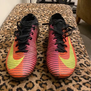 Nike Mercurial fotbollsskor - Säljer ett par Nike Mercurial fotbollsskor i svart, orange och gul. Skorna har snörning och en strömlinjeformad design med tydliga Nike-loggor. Fortfarande bra kvalite, med bra grepp!