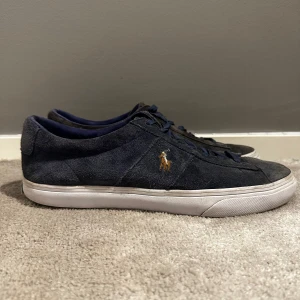 Mörkblå sneakers från Polo Ralph Lauren - Snygga mörkblå sneakers från Polo Ralph Lauren med en stilren design. Skorna har en ovandel i mocka och en vit sula i gummi. Storlek 43