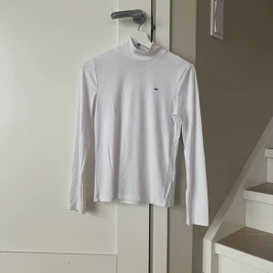 Vit ribbad polotröja från Tommy Jeans - Säljer en stilren vit ribbad polotröja från Tommy Jeans. Tröjan har långa ärmar och en liten logotyp på bröstet. Knappt använd.