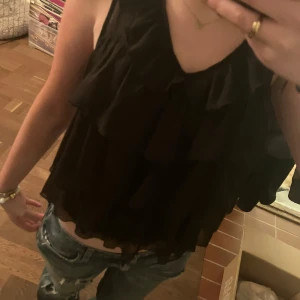 Svart volanglinne - Snygg svart ärmlös linnetopp med volanger. Perfekt för en stilren look. Passar bra till jeans eller kjol. Dock avklippt så är lite sliten i botten