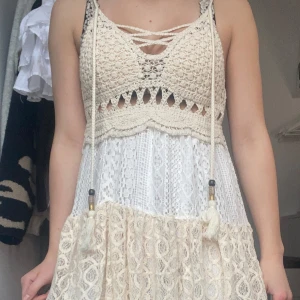 Beige klänning med knytband - Charmig beige klänning med knytband framtill. Den har en vacker virkad överdel och smala axelband. Perfekt för sommarens varma dagar.