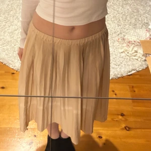 Beige kjol - Säljer en stilren ljusrosa kjol med veckad design. Kjolen har en elastisk midja för bekväm passform och faller vackert i en längre modell. Perfekt för en chic och avslappnad look. Är i strl 130 och jag är ca 160 cm. Den är mer rosa i verkligheten.