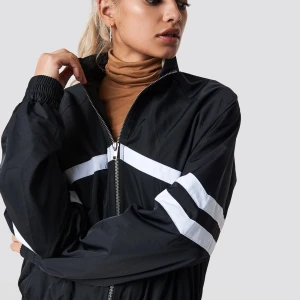 Svart vindjacka med vita ränder - Snygg svart vindjacka med vita ränder över bröstet och ärmarna. Jackan har en dragkedja framtill och elastiska muddar vid ärmslut och nederkant. Perfekt för lite blåsigare dagar!☺️Säljes på grund av att den inte kommer till användning. Bra skick. Ordinarie pris 399 kr. 