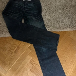 Blå gröna med glittrig yta - Snygga blåa gröna jeans med en glittrig yta som ger en unik look. De har en rak passform och är perfekta för att sticka ut. Jeansen har en klassisk design med dragkedja och knapp framtill. Inga fickor bak!