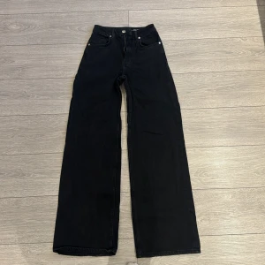 Svarta jeansbyxor - Snygga svarta jeansbyxor med hög midja och breda ben. Klassisk femficksdesign med knapp och dragkedja framtill. Perfekta för en stilren look.