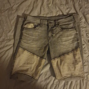 Grå jeans från True Religion - Priset kan variera. Snygga grå jeans från True Religion med unika randiga detaljer på benen. De har en klassisk femficksdesign och en knappgylf. Perfekta för en avslappnad stil med en touch av edge.