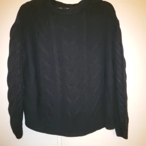 Svart stickad tröja - Säljer en svart stickad tröja med kabelstickat mönster. Tröjan har långa ärmar och en rund halsringning. Perfekt för kyligare sommardagar.